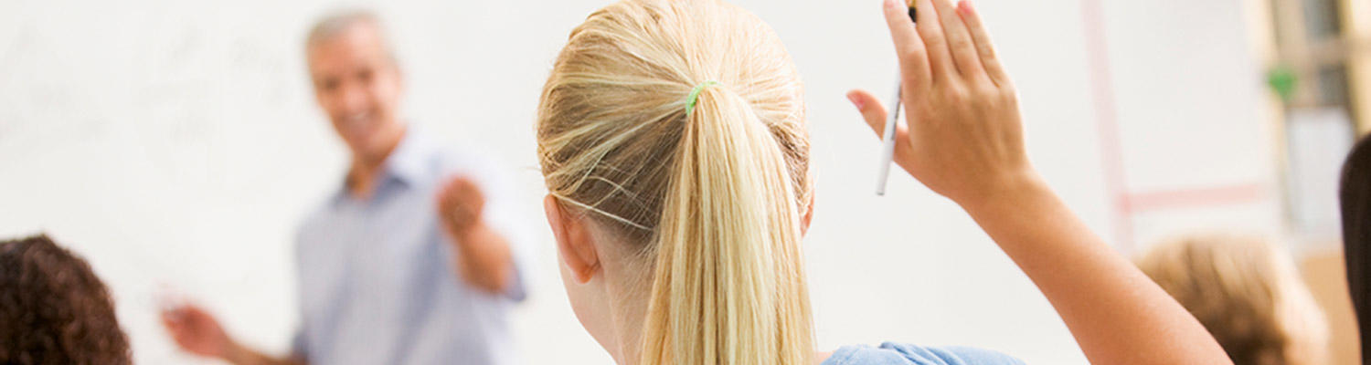teacher calling on a girl with her hand raised in a classroom
