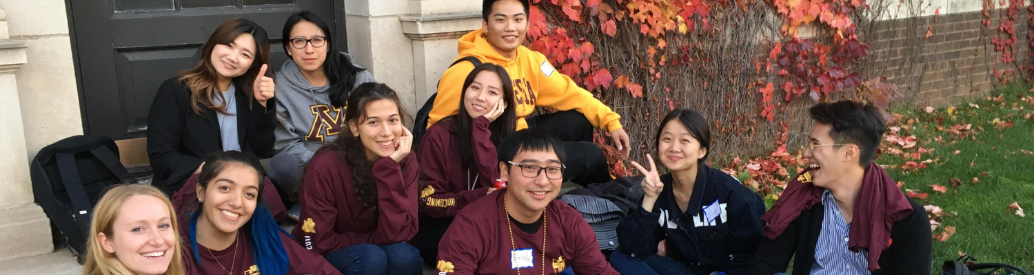 A group of MELP students dressed in maroon and gold, sits together in the steps of a UMN building