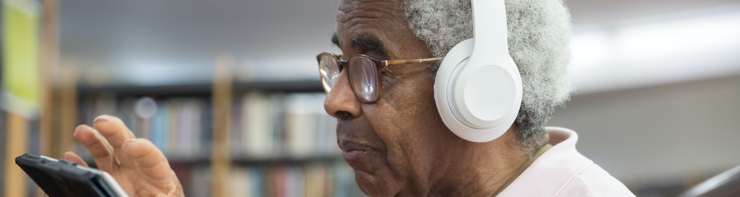 older man wearing large white headphone and working intently on an iPad