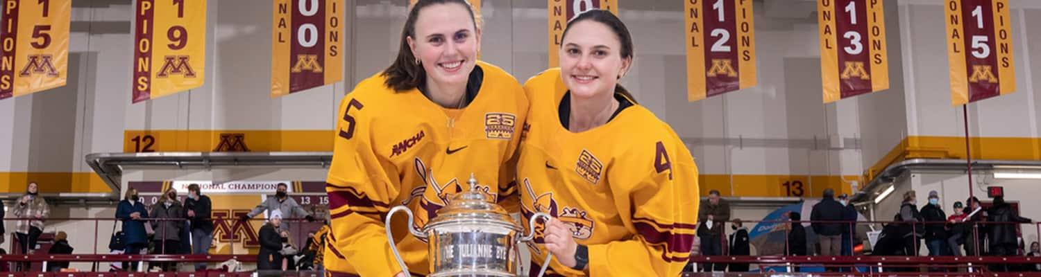 Audrey and Madeline Wethington in their Gopher hockey uniforms holding the Julianne Bye Cup.