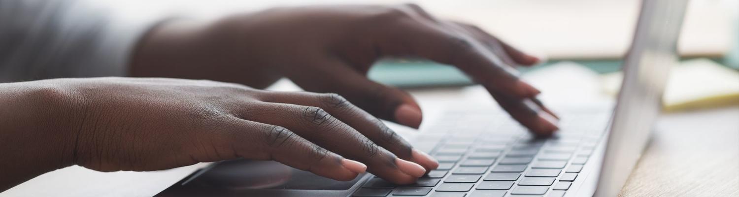 The hands of a Black woman typing on a silver laptop