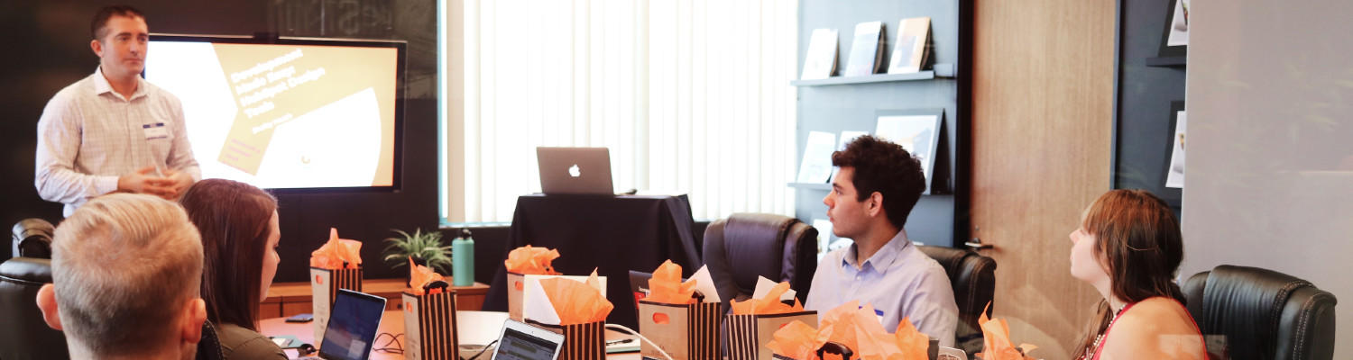 a man presenting before a meeting room of people with laptops and gift bags