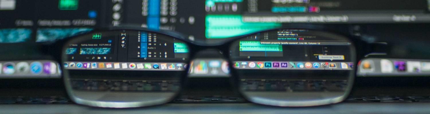 image of blurry computer monitors coming into focus behind a pair of glasses