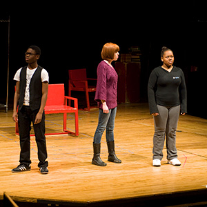 Three students on stage rehearsing a play