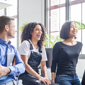 Two women and a man sit in a meeting, talking cheerfully.